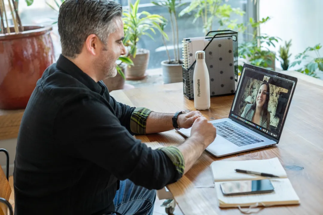 A consultant on a one-to-one video call, taking notes beside the laptop