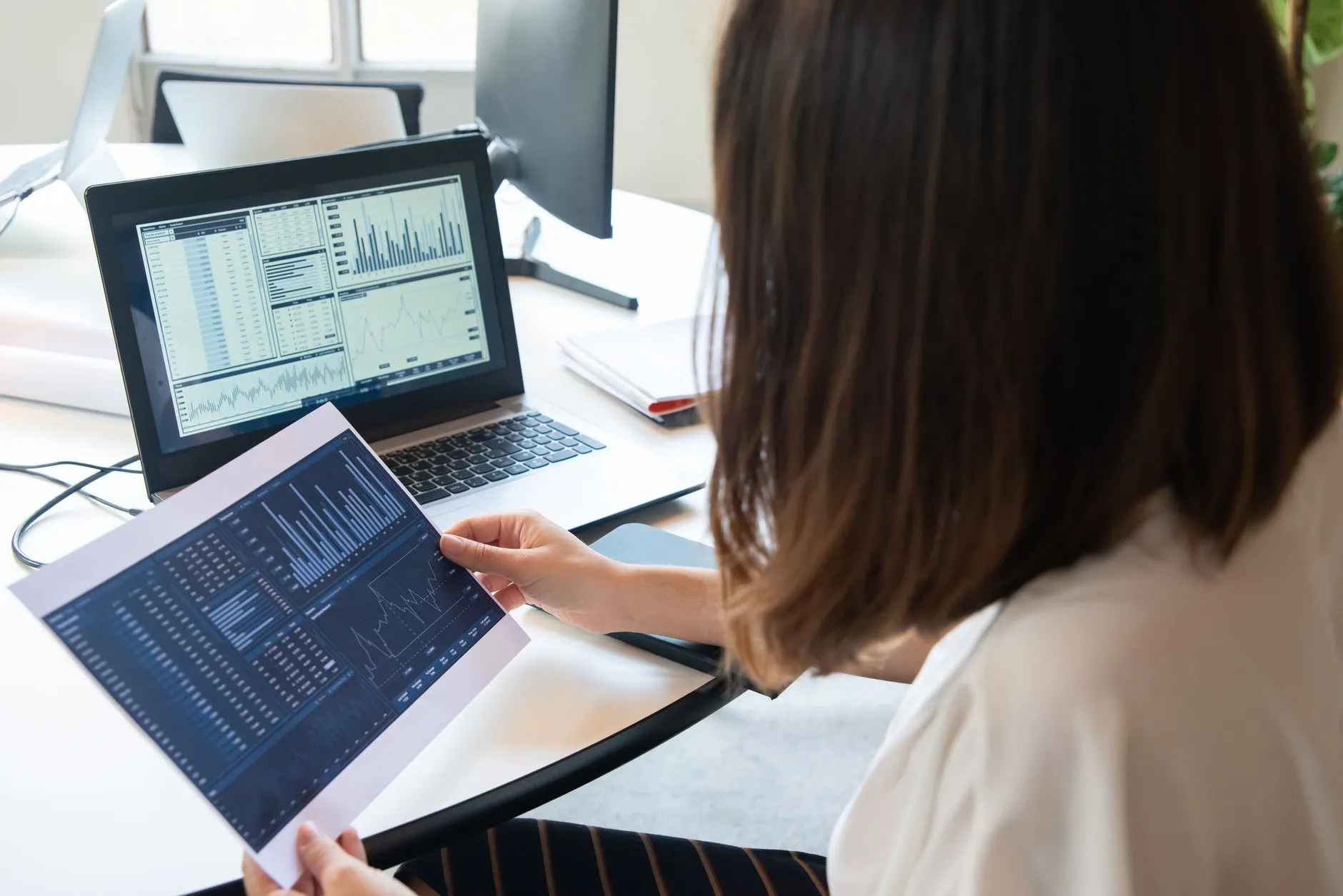 Person reviewing analytics charts on a laptop screen and printed report