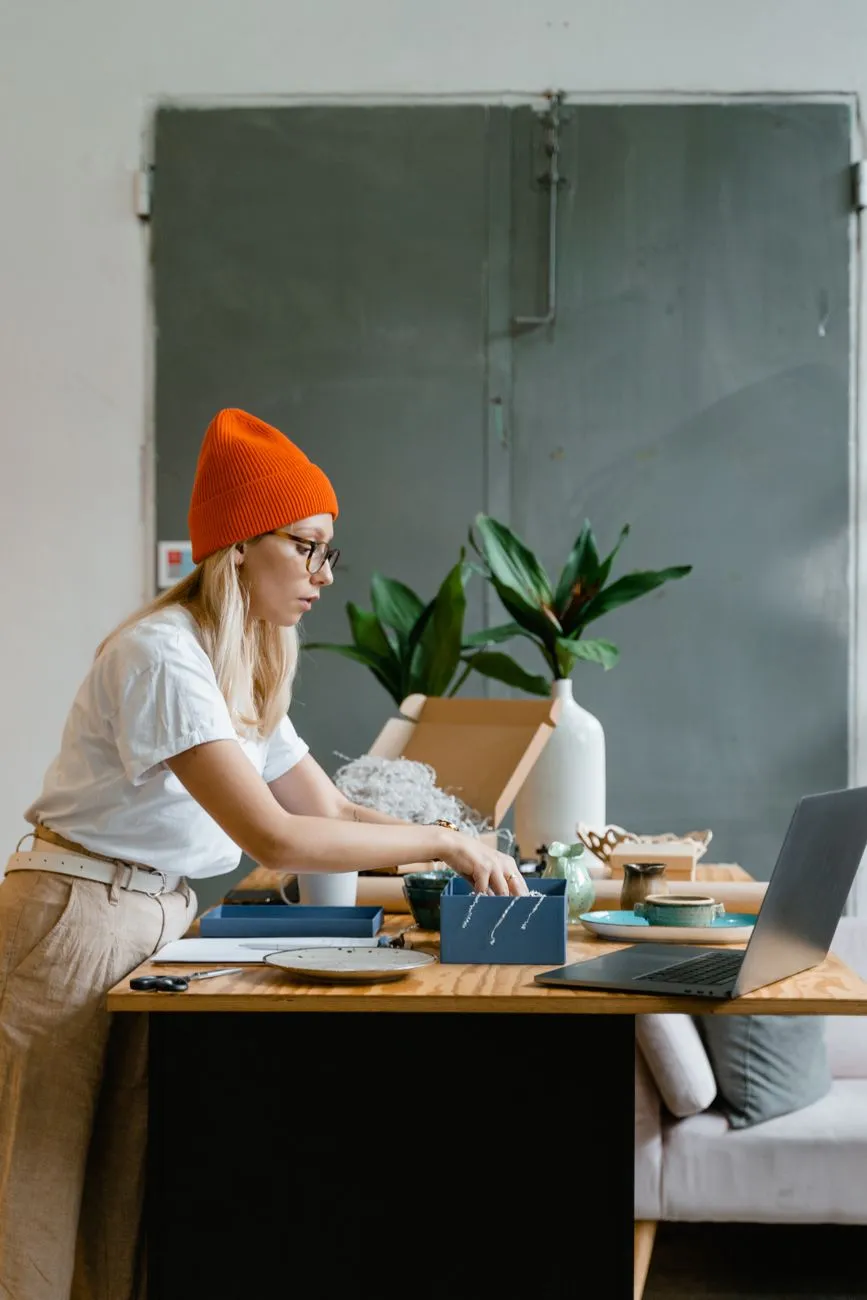 Small business owner packing an order with a laptop open on the desk